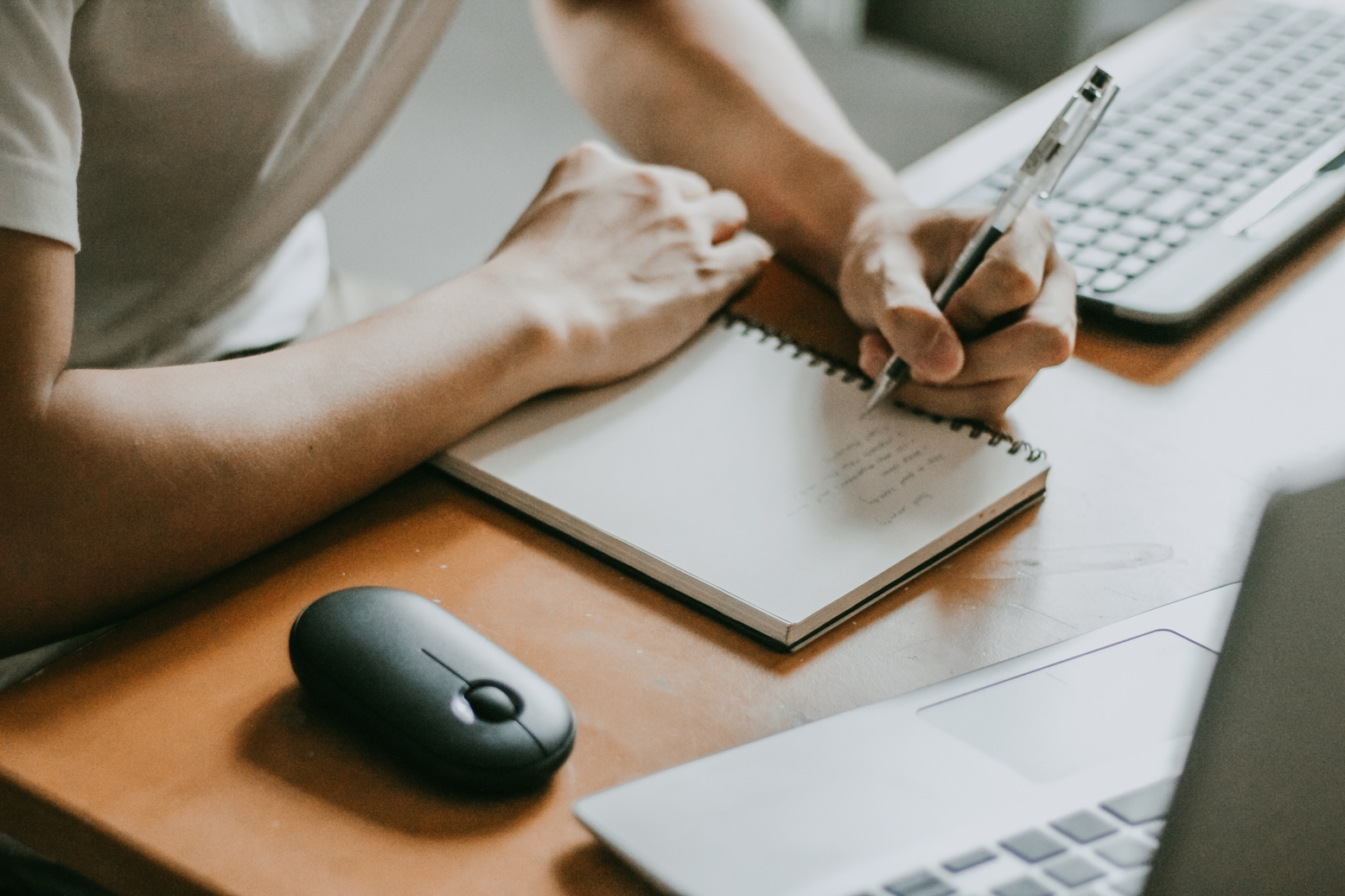 Man Writing on a Notebook and Laptop on the Table